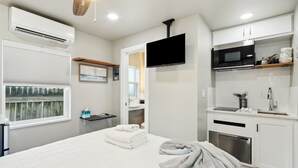 A modern hotel room with a bed, a flat-screen TV, a kitchenette, and a bathroom visible through an open door. - Beach 5 Villas - Immaculate 300 steps from the Ocean (Fernandina Beach)