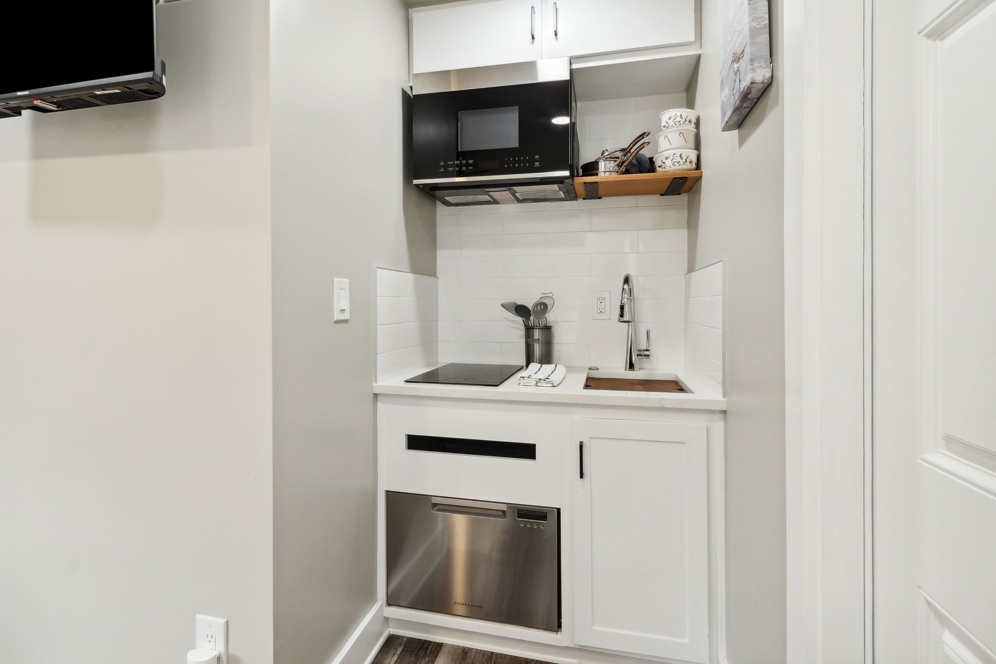 A compact kitchen with white cabinetry, a stainless steel dishwasher, a black microwave, and a built-in oven.