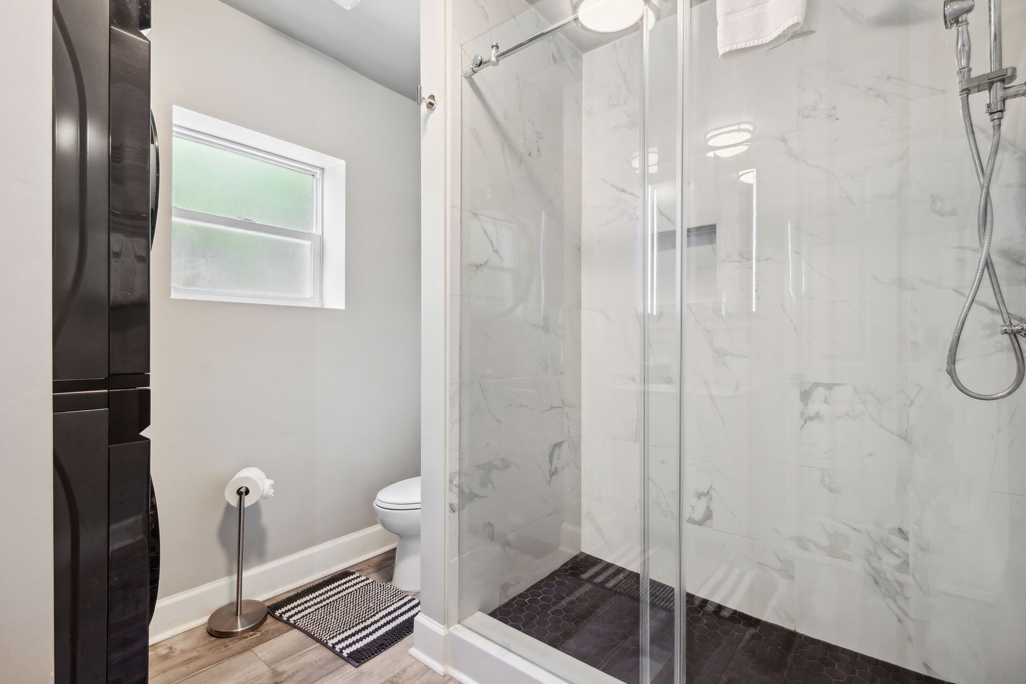 Un baño moderno con ducha de vidrio, inodoro y refrigerador negro.