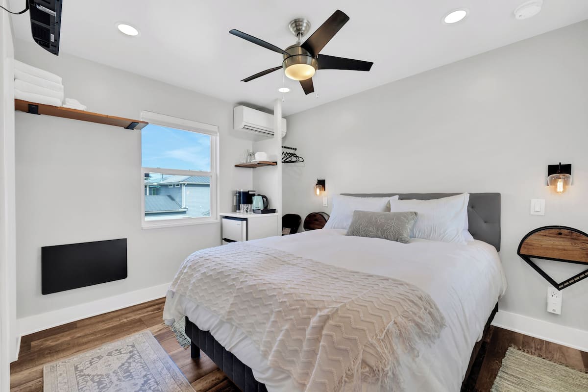 A modern bedroom with a large bed, a ceiling fan, a window, and a built-in shelf.
