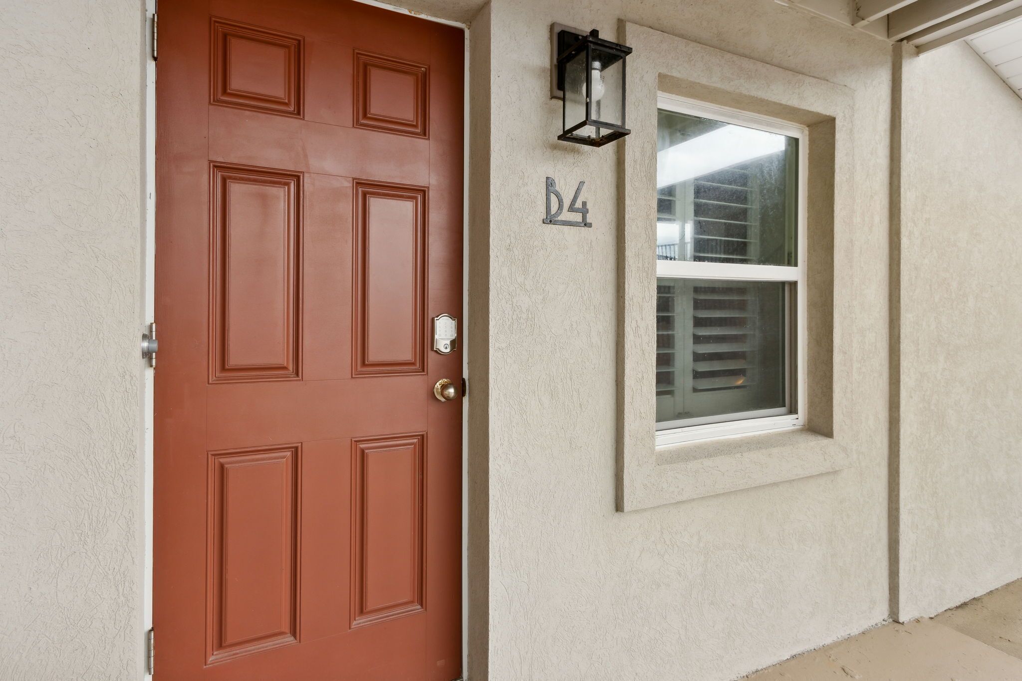 A brown door with a number 'D4' above it, a window with blinds, and a wall-mounted light fixture.