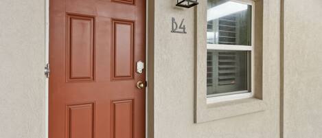 A brown door with a number 'D4' above it, a window with blinds, and a wall-mounted light fixture.