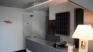 A hotel reception area with a reception desk, a signboard with hotel information, a wall-mounted shelf, and a lamp. - Hôtel Le Rohu (Sene)