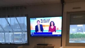 A conference room with a TV displaying a news program, a table with breakfast items, and seating. - Hôtel Le Rohu (Sene)