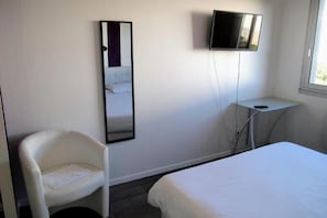 Una habitación de hotel con cama, una silla, televisor montado en la pared y una mesita.