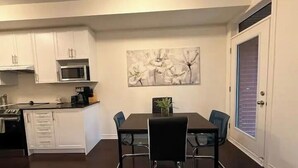 Una cocina compacta con gabinetes blancos, un microondas y un comedor con una mesa y sillas negras.