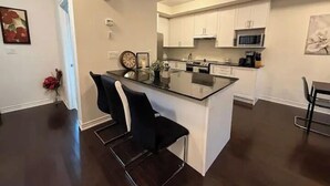 Una cocina moderna con armarios blancos, una isla central y un comedor con una silla negra.