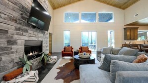 A spacious living room with a stone fireplace, a large flat-screen TV, and a high ceiling. - Pets | Heated Pool | Game Room | Sleeps 36 (Broken Bow)