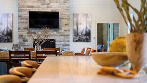 A dining area with a stone wall, a flat-screen TV mounted above a fireplace, and artwork on the walls. - Pets | Heated Pool | Game Room | Sleeps 36 (Broken Bow)