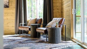 A cozy room with wooden walls, two leather chairs, a small table, and a large window with curtains. - Pets | Heated Pool | Game Room | Sleeps 36 (Broken Bow)