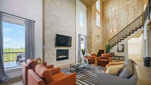 A spacious living area with a fireplace, a staircase, and a balcony with outdoor furniture.