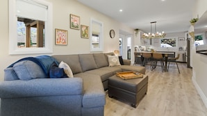 Una sala de estar moderna con un sofá modular, un reposapiés y un comedor con taburetes de bar.