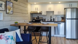 A modern kitchen with white cabinets, a stainless steel refrigerator, and a wooden dining table with bar stools.