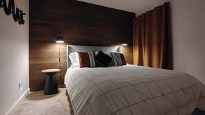 A bedroom with a large bed, two bedside lamps, a wooden headboard, and a small round table.