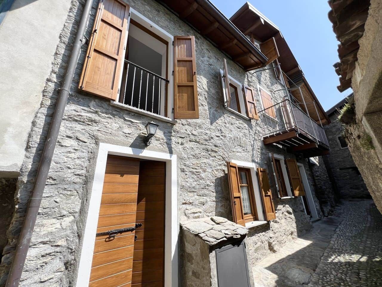 Un bâtiment en pierre avec des volets en bois, un balcon et un chemin pavé.