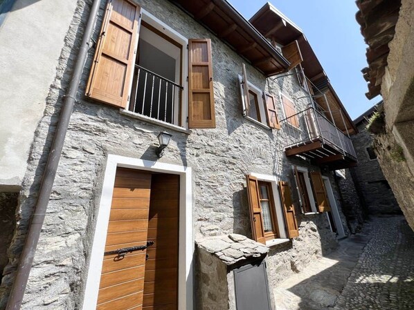 A stone building with wooden shutters, a balcony, and a cobblestone path.