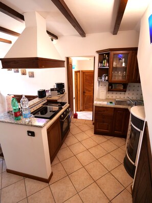 A kitchen with a central island, wooden cabinets, a stove, and a built-in oven. - Casa Marie, a rustic natural stone home with a lake view and a rooftop terrace (Vercana)