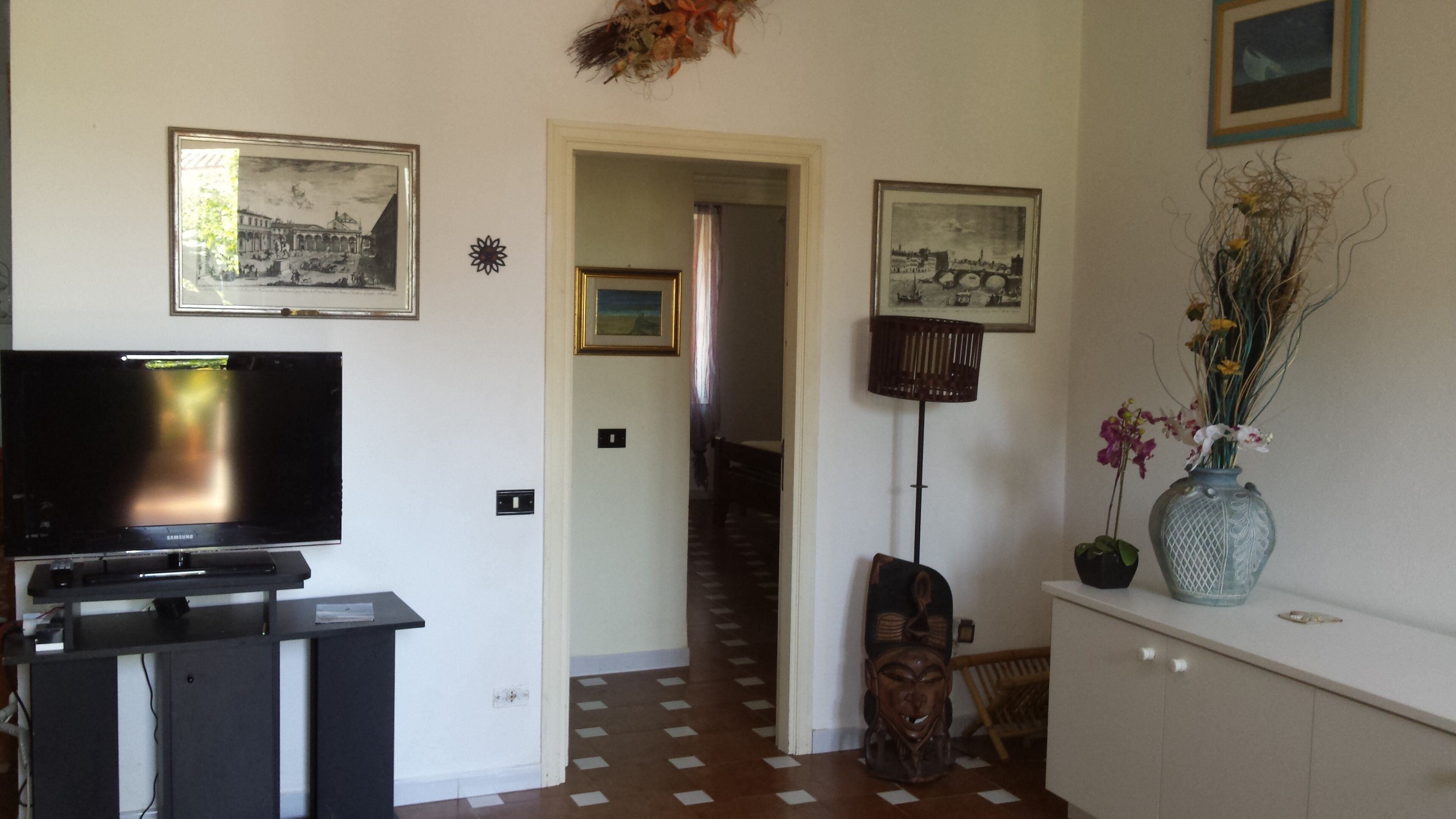 A living room with a flat-screen TV, a wooden cabinet, and a vase with flowers.