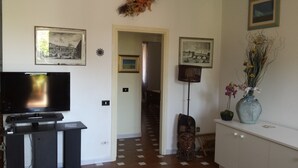A living room with a flat-screen TV, a wooden cabinet, and a vase with flowers. - Sardinia! Budoni 1 km from the wonderful beach of Sant'Anna: 4 beds (Tanaunella)