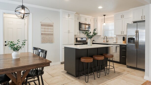 A modern kitchen with white cabinets, a central island with stools, a microwave, and a stainless steel refrigerator.