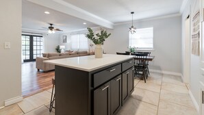 A modern kitchen with a central island, dark cabinetry, and a dining area with chairs and a table.