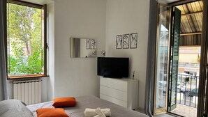 A hotel room with a bed, a television, a window with a view of trees, and a door leading to an outdoor area.