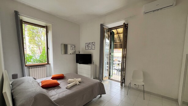 A modern hotel room with a bed, a TV, a small table, and a window with curtains.