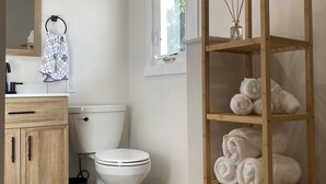 A modern bathroom with a toilet, a wooden cabinet, a towel rack, and a wooden shelf with towels. - Airport bungalow  (Coraopolis)