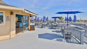 An outdoor seating area with umbrellas, a beach view, and a sign indicating a restaurant.