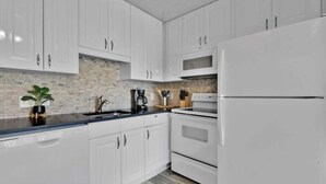 A modern kitchen with white cabinets, a black countertop, a stainless steel refrigerator, and a built-in oven.