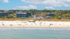 A beachside hotel with multiple buildings, a sandy beach, and a forested background.