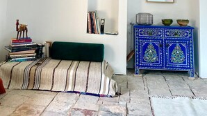 Una habitación con un sofá verde, una pequeña estantería, un aparador decorativo y un espejo en la pared.