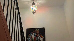 Una escalera con barandilla negra, un lámpara colgante de colores y un cuadro en la pared.