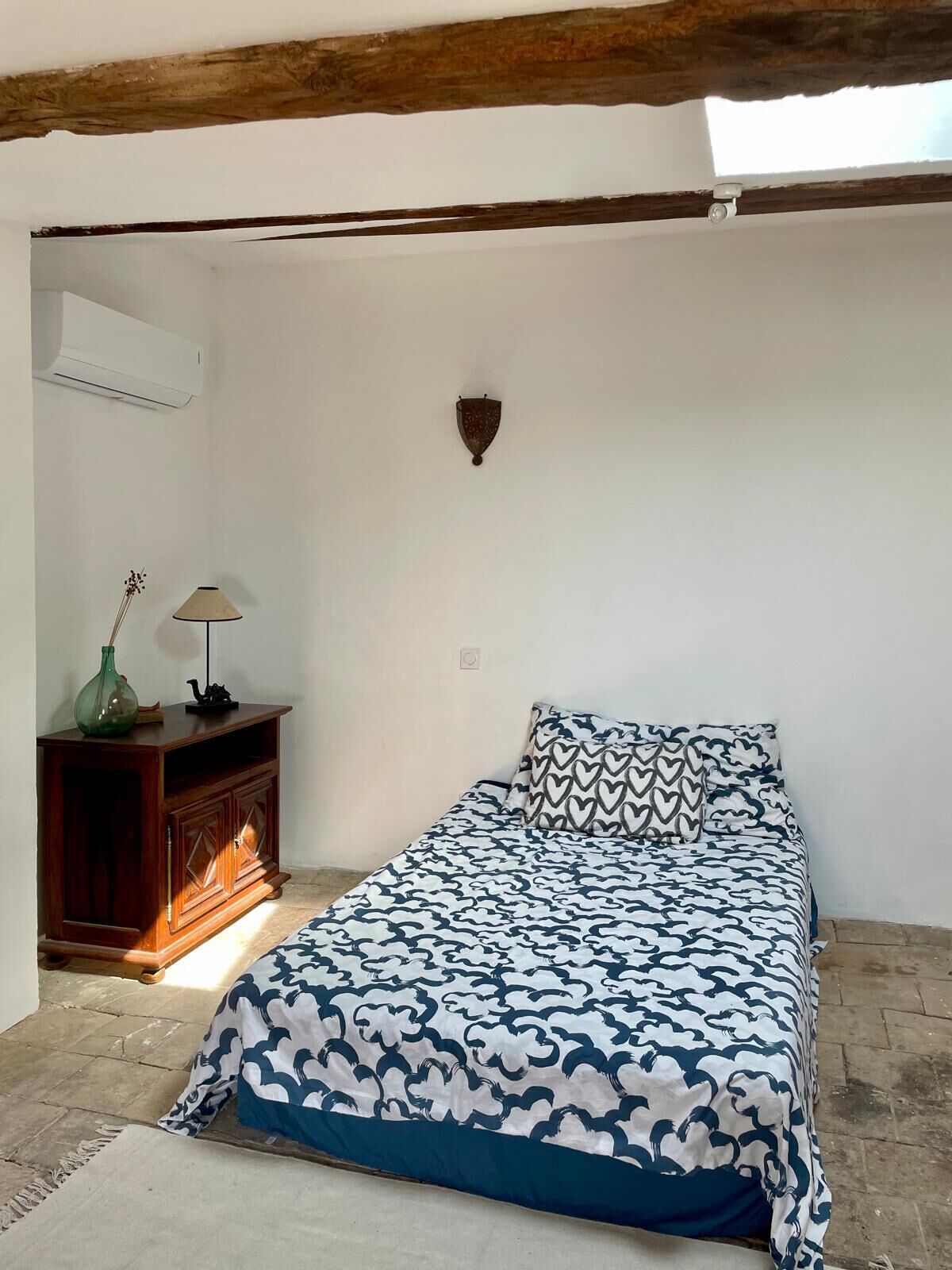 Un dormitorio con cama, mesita de noche, lámpara y aplique de pared.