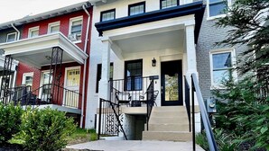 A residential building with a front porch, a staircase, and a brick pathway leading to the entrance.