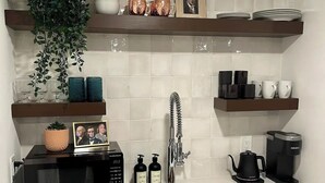 A kitchen with a microwave, coffee maker, sink, and various decorative items on shelves.