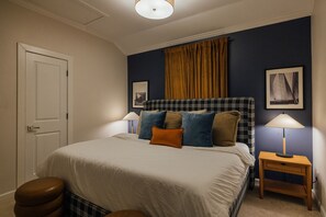Quarto com cama, duas mesas de cabeceira, porta e janela com cortinas.