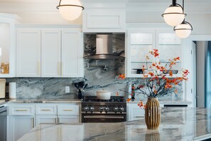 A modern kitchen with white cabinetry, a marble backsplash, a central island, and a vase with flowers. - LakeFront with Pool! HotTub! Game Room! Sleeps 20+

 (Hot Springs)