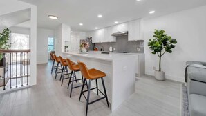 A modern kitchen with white cabinets, a central island with bar stools, and a potted plant. - Sea Destin - Private BeachFront Townhouse (Destin)