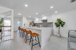Una cocina moderna con armarios blancos, una isla central con taburetes altos y una planta en maceta.