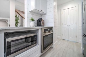 A modern kitchen with built-in appliances, white cabinetry, and a wooden staircase.