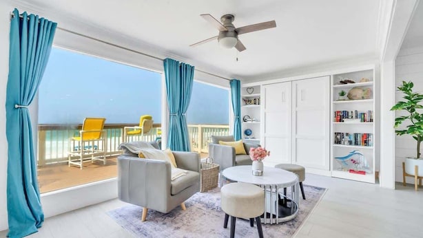 A bright room with a balcony, a ceiling fan, a round table, and a bookshelf. - Sea Destin - Private BeachFront Townhouse (Destin)