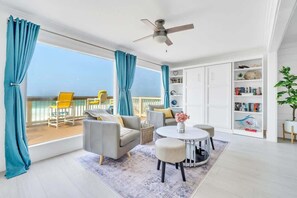 Habitació lluminosa amb un balcó, un ventilador de sostre, una taula rodona i una prestatgeria.