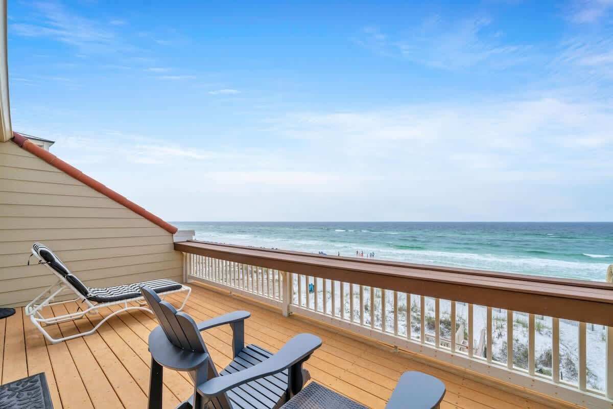 A wooden deck with lounge chairs and a table overlooking the ocean.