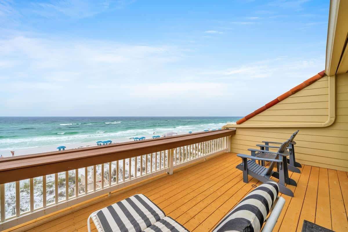 A wooden deck with a view of the ocean, a lounge chair, and a table with chairs.