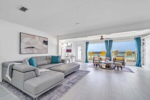 A modern living room with a grey sectional sofa, a round coffee table, and a view of the sea through large windows.