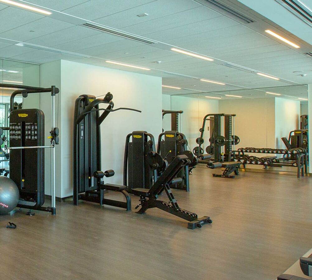 Un gimnasio con diferentes máquinas de ejercicio, espejos en las paredes y suelo de madera.