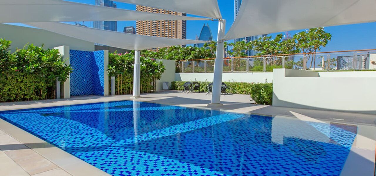 Ein Swimmingpool mit blauem Mosaikfliesenmuster, umgeben von weißen Wänden und Grünpflanzen.