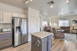 A modern kitchen with stainless steel appliances, a dining area with a sofa and armchairs, and a ceiling fan.