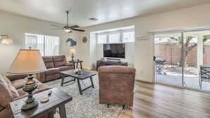 A living room with a sofa, armchair, coffee table, lamp, TV, and a sliding glass door leading to a patio. - Starling Mesa | Extended Stay Modern Vegas (North Las Vegas)